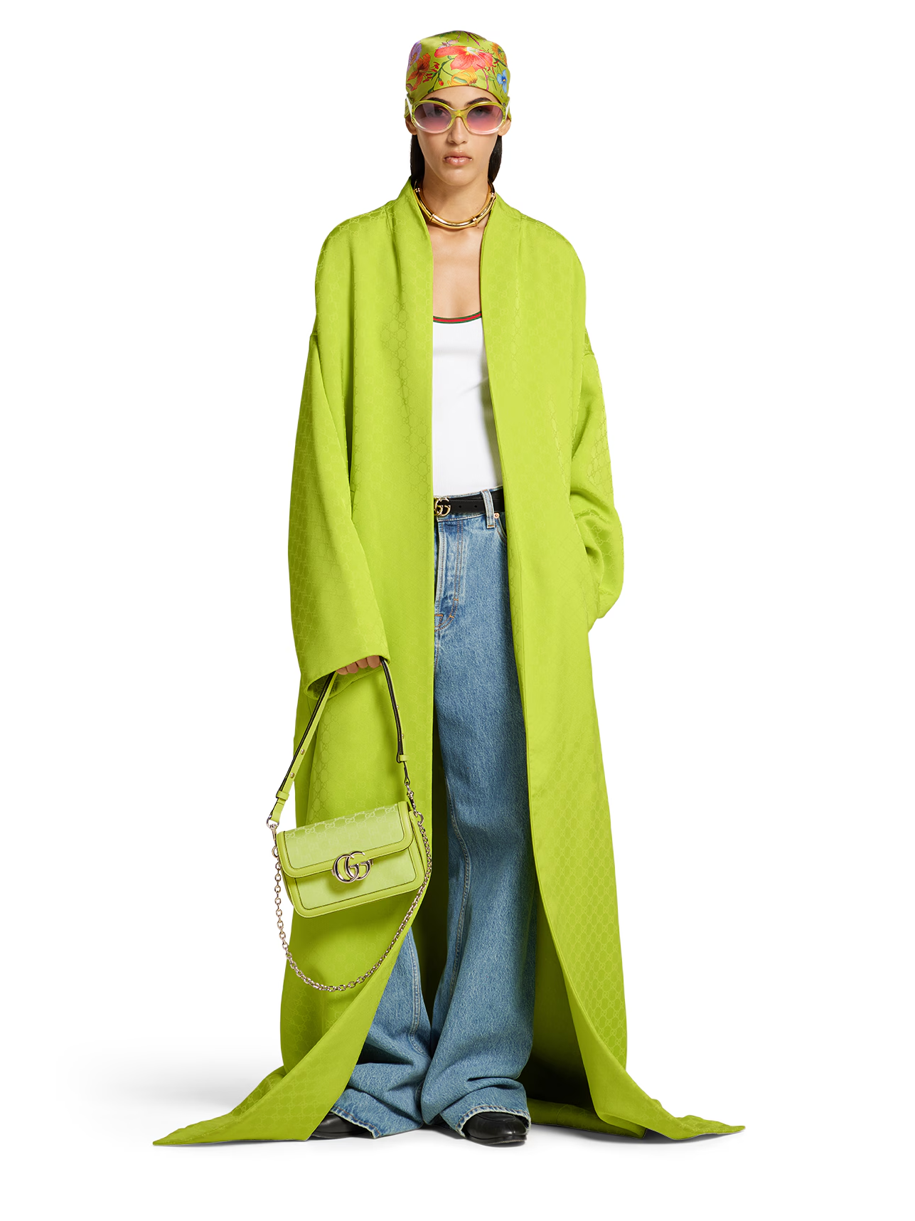 A model wearing Gucci 25ss look, a vibrant lime green long coat over a white tank top and baggy blue denim, holding a small lime green handbag and accessorized with a floral headscarf and sunglasses.