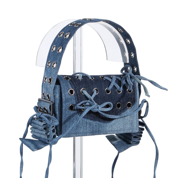 A stylish upcycled denim handbag featuring eyelet details and knotted accents, displayed on a clear pedestal.
