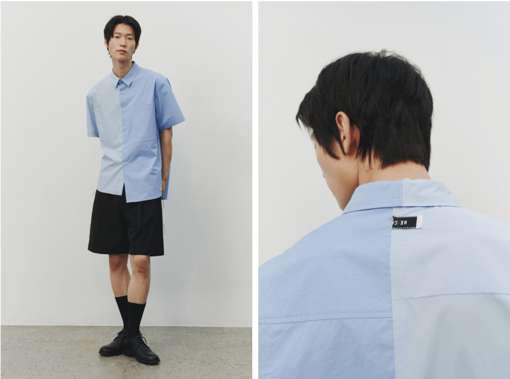 A model wearing an upcycled two-tone short-sleeve button-up shirt with one side in light blue and the other in a slightly darker shade, paired with black shorts and socks, showcasing a contemporary Korean fashion aesthetic.