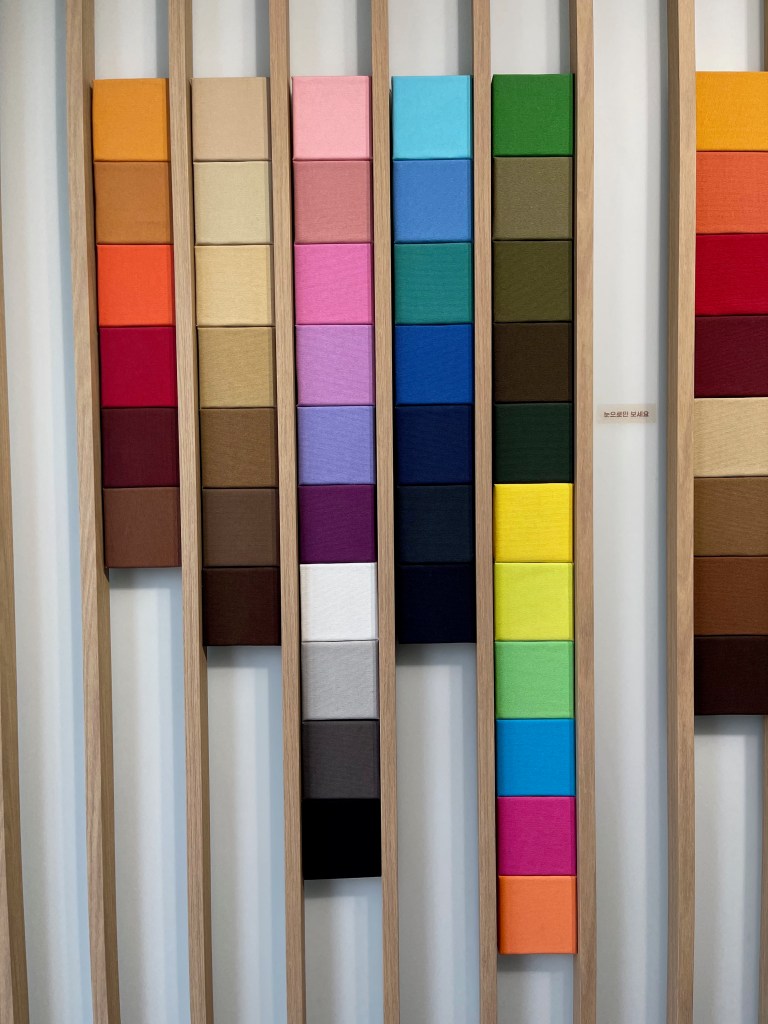 A vertical display of various fabric swatches arranged in a grid, showcasing a wide range of colors including orange, pink, green, and blue in sinseol-dong material market.