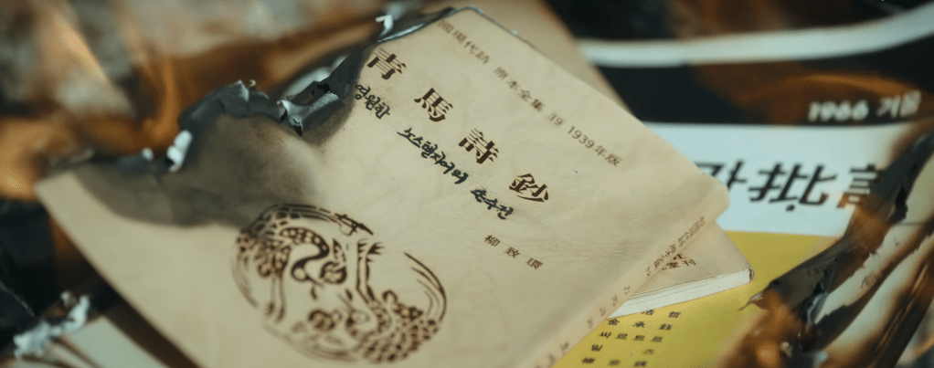 A close-up of partially burned books on a table, showcasing Korean text and vintage packaging, symbolizing cultural loss and historical context.