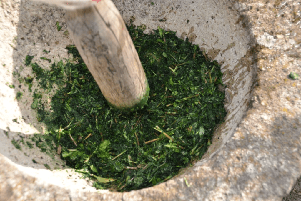 A wooden pestle grinding fresh green Jjok in a stone mortar.