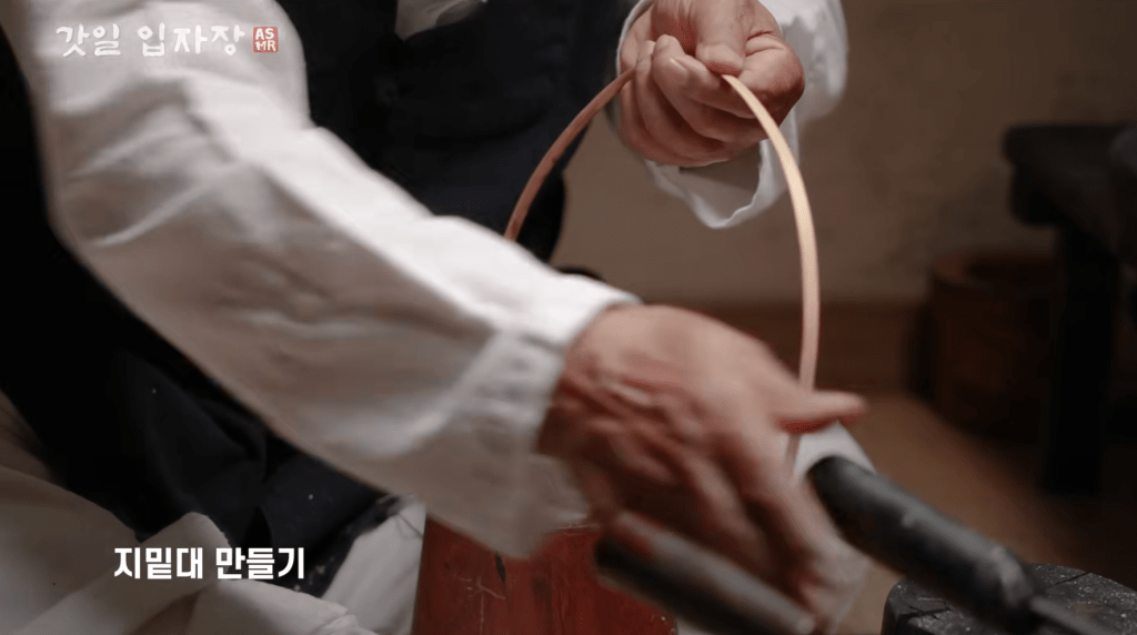 A person shaping a bamboo wire in a traditional gat workshop, showcasing craftsmanship.