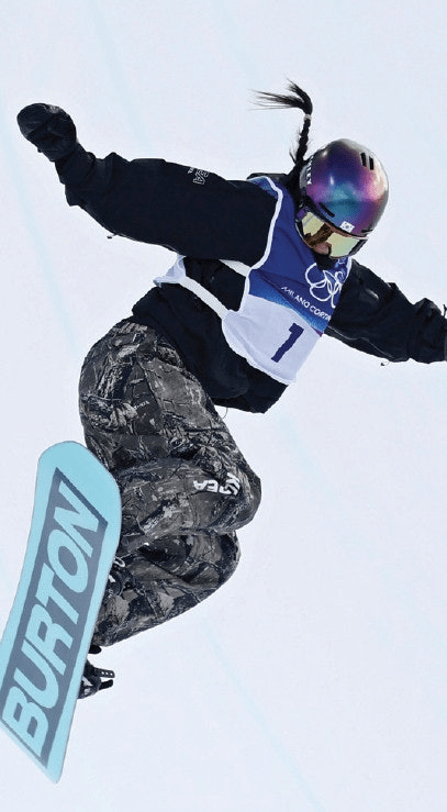 A snowboarder Choi Gaon performing a trick in mid-air during 2026 Milano cortina Winter Olympics, wearing a black jacket, camouflage pants, and a colorful helmet.