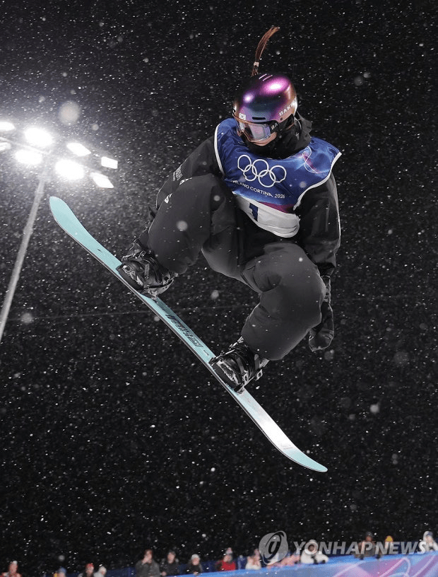 A snowboarder Choi Gaon performing an impressive jump in a snowy environment during the 2026 Milano cortina winter Olympics, wearing a helmet and goggles.