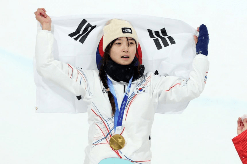 In 2026 Milano Cortina Winter Olympics, Choi Gaon is celebrating with a South Korean flag and wearing a winter jacket, holding a gold medal around her neck.