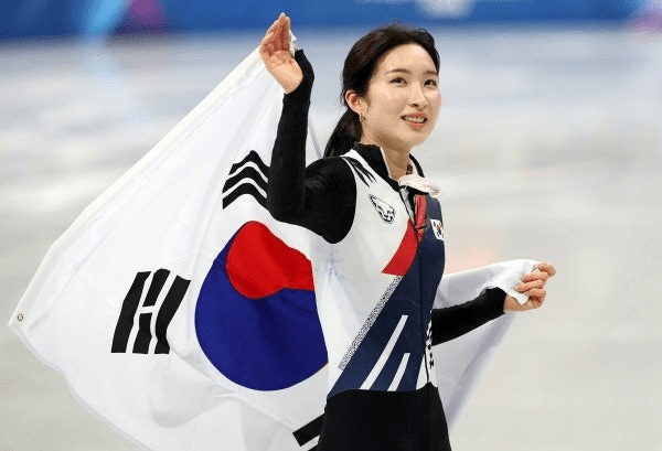 Kim Gil-li speed skater in a black and white costume, smiling and waving a South Korean flag on the ice rink.