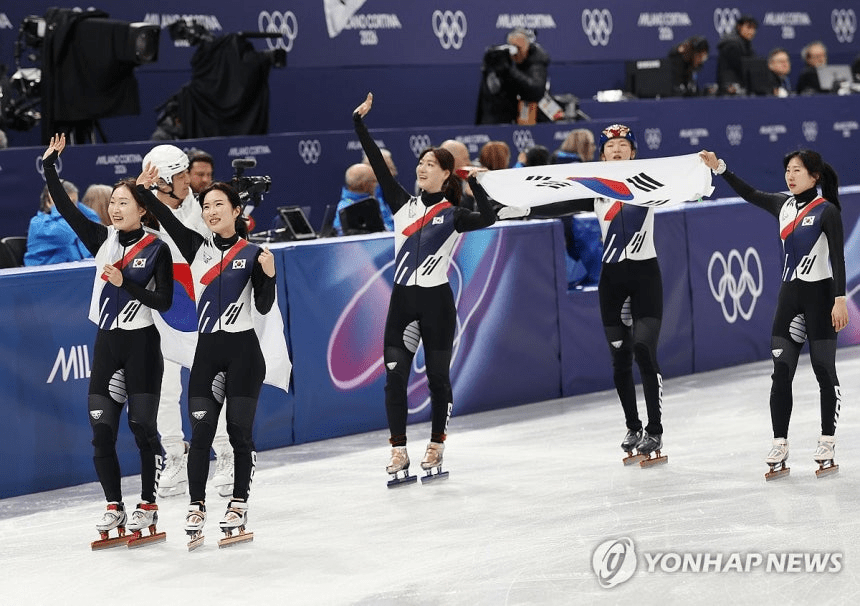 A gold medal winner of South Korean  speed skate team celebrating on the ice during 2026 Milano cortina winter olympics, holding korean flags and expressing joy.
